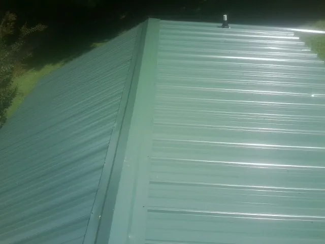 New green metal panels meeting at the ridge of a roof — Flat Roof Repair work by our crew in South Bend