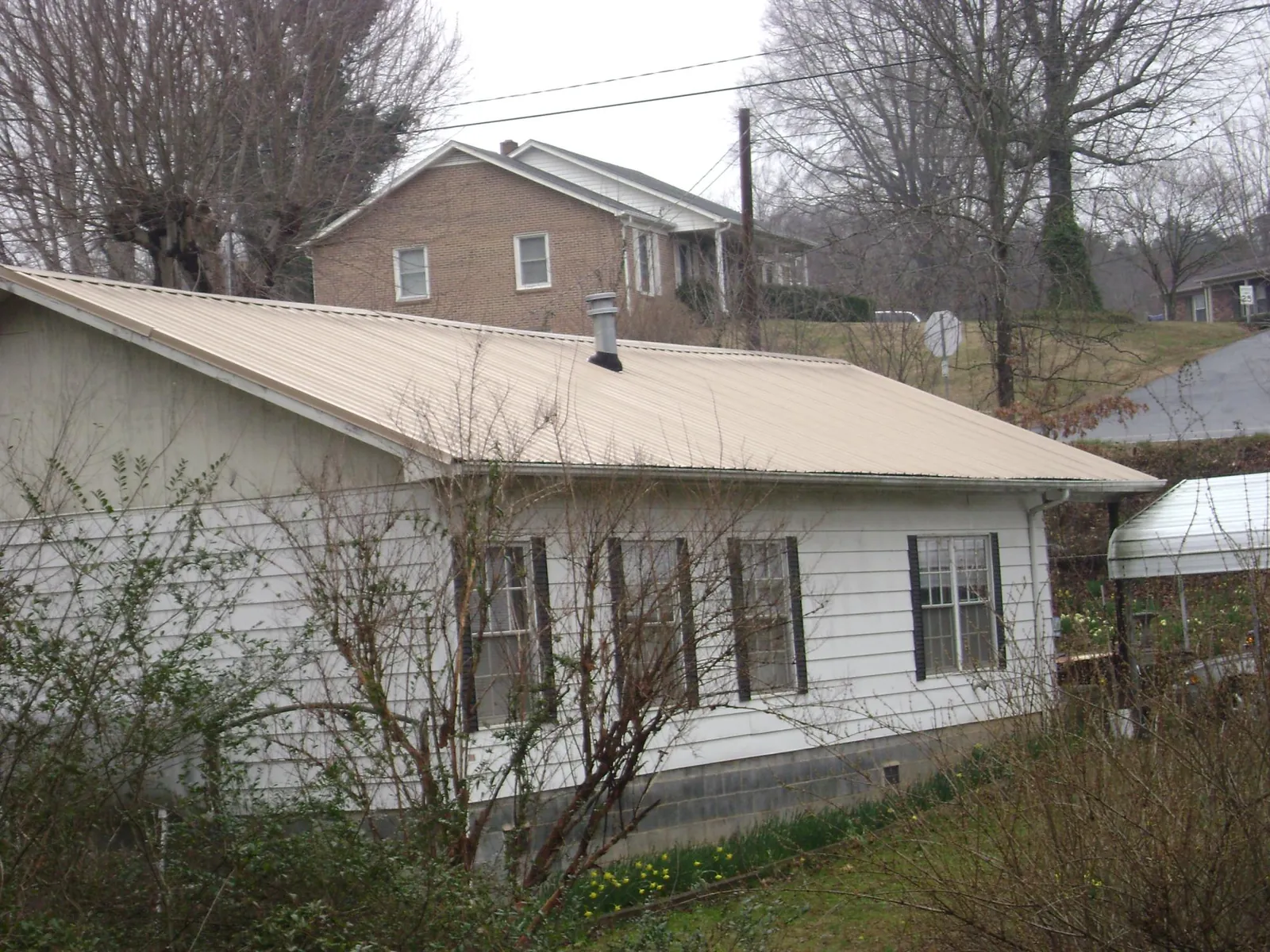 Tan metal roof on a white sided house set into a hillside — Commercial Roofing by Roofing Brothers in South Bend